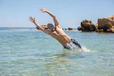 Genç yakışıklı sarışın adam denize dalıyor.