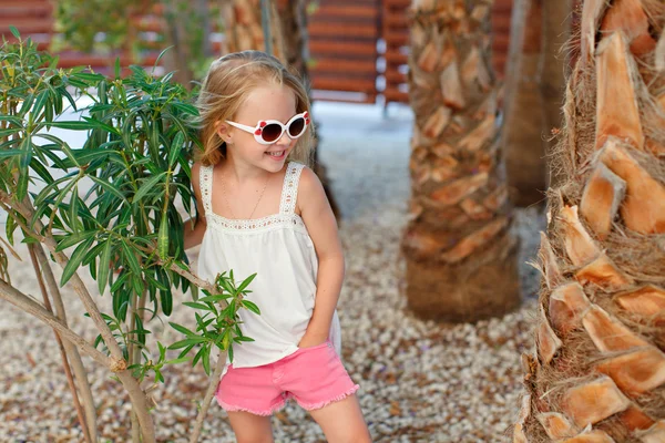 Charmant blond meisje in roze shorts en zonnebrillen staan in de buurt — Stockfoto