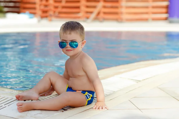 Маленький очаровательный пухлый мальчик в очках, сидящий на бассейне — стоковое фото