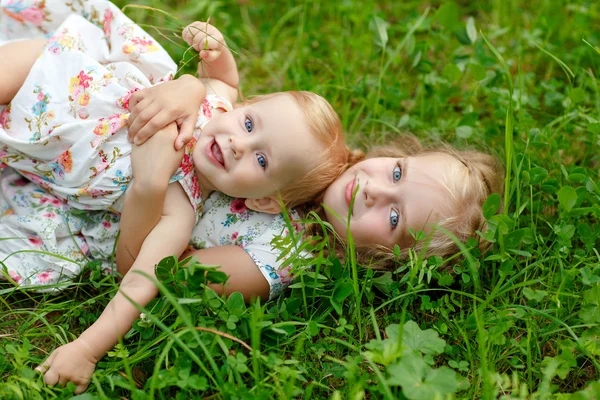 Twee charmante zusters blond meisje knuffelen en lachen, liggend op — Stockfoto