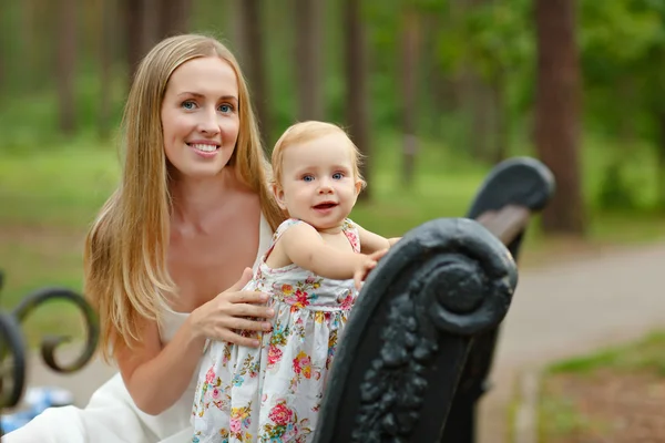 De slanke blonde moeder en dochter zittend op een bankje in de — Stockfoto