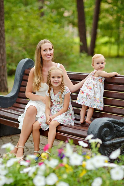 Uma mãe esbelta e duas filhas loiras sentadas em um banco em — Fotografia de Stock