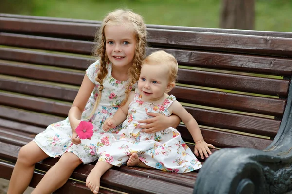 Two charming sisters blonde girl sitting on a bench in the summe