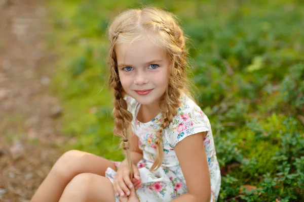 Porträtt av charmiga flicka med blonda flätor, på gräset i — Stockfoto