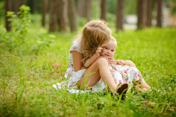 Twee charmante zusters blond meisje knuffelen en lachen op de gra — Stockfoto