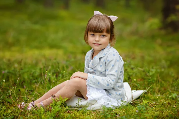 Charming baby girl with brown eyes is sitting on the grass in th — Stock Photo, Image