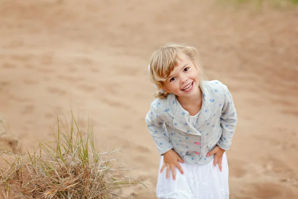 Little charming girl with brown eyes on a background of sand smi — Stock Photo, Image