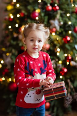 Küçük kız çocuk kırmızı kazaklı bir hediye yılbaşı ba üzerinde tutan