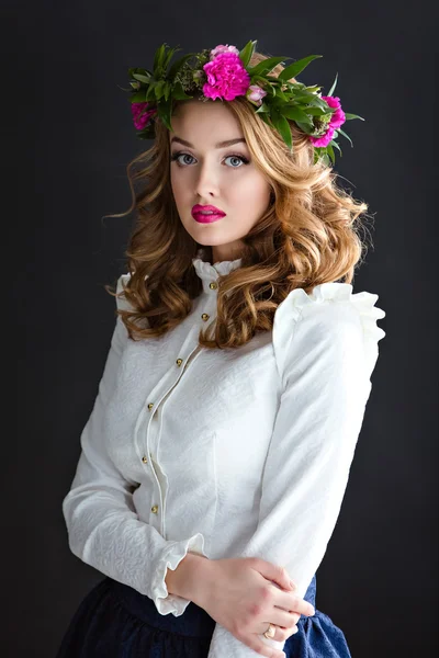 Portret van een mooi sensuele meisje in een elegante witte blouse met een krans van bloemen op zijn hoofd, op een donkere achtergrond in Studio — Stockfoto