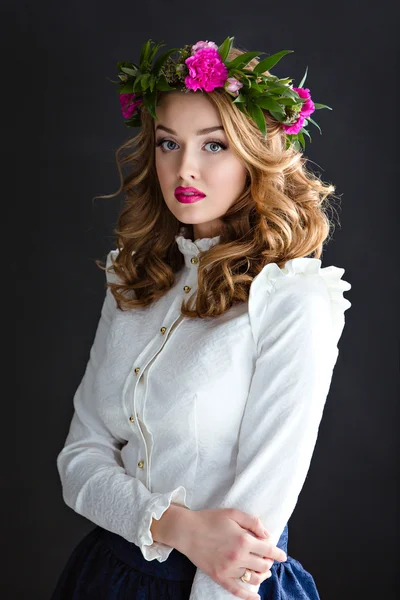 Porträt einer schönen sinnlichen Mädchen in einer weißen eleganten Bluse mit einem Blumenkranz auf dem Kopf, auf einem dunklen Hintergrund im Studio — Stockfoto