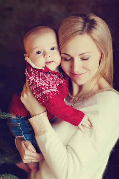 Mamá rubia en suéter blanco besa niño el niño en el rojo — Foto de Stock