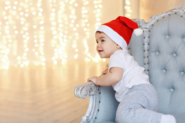 Pequeno menino encantador em chapéus vermelhos de Papai Noel sentado em uma cadeira aga — Fotografia de Stock