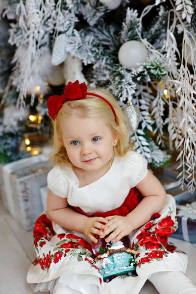 Babymeisje charmante blonde in een rode jurk zitten naast een — Stockfoto