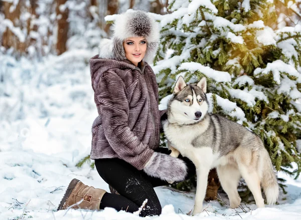 A menina de casaco cinza sentada ao lado de um cão husky cinza no inverno — Fotografia de Stock