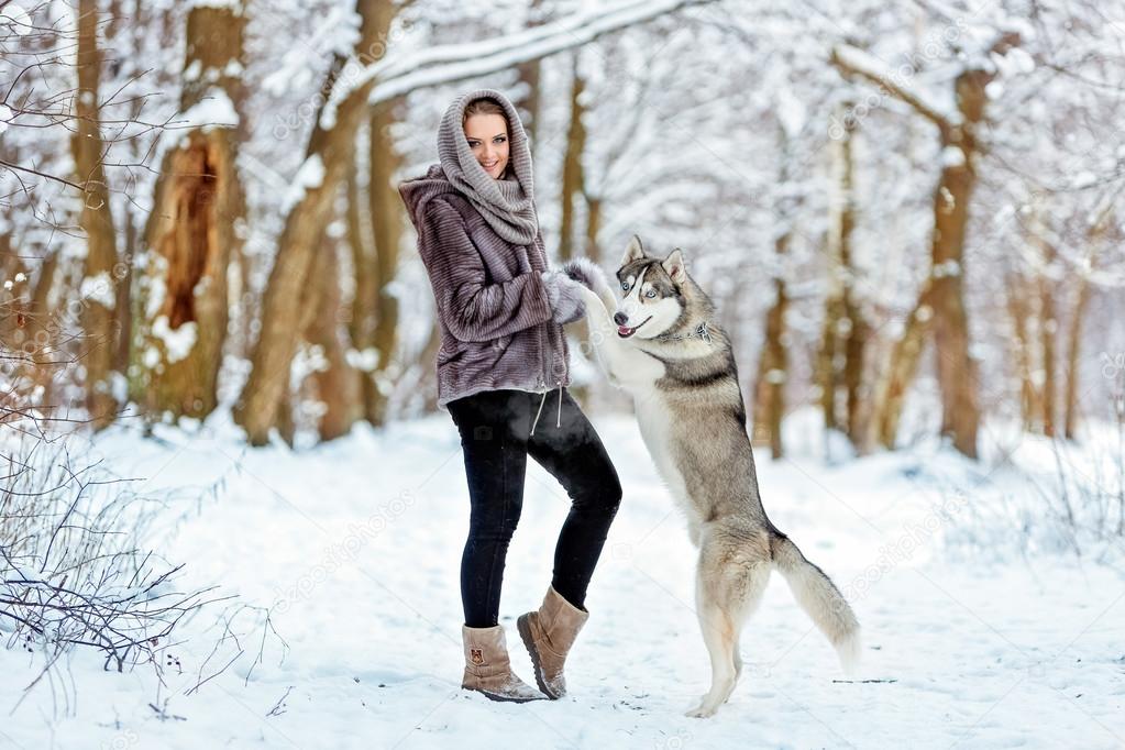 Cute girl keeps his paws dog husky on the background of the forest in winter
