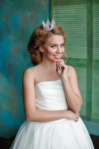 Close-up πορτρέτο του ένα χαμογελαστό ξανθιά κοπέλα με πλήρη χείλη, φορώντας ένα λευκό φόρεμα και ένα στέμμα στο κεφάλι του, σαν πριγκίπισσα — Φωτογραφία Αρχείου
