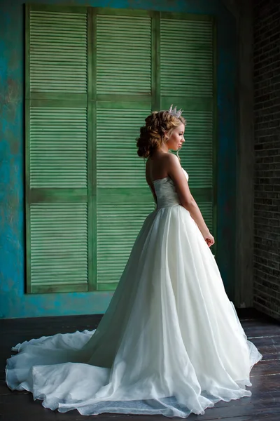 Portrait of a young blonde woman with chic thick hair, wearing a white dress and a crown on his head, looking toward the window, a full-length in profile — Stock Photo, Image