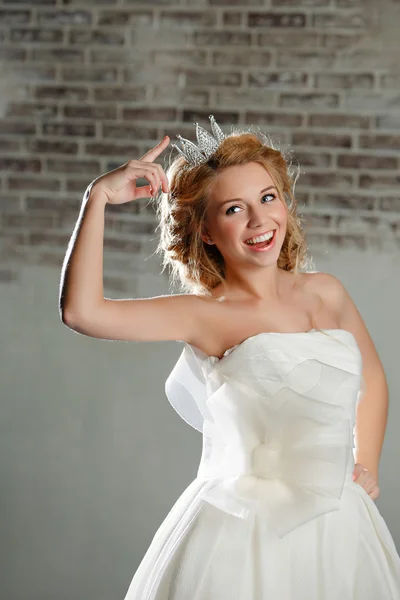 Portrait d'une jeune femme blonde aux lèvres pleines, portant une robe blanche et une couronne sur sa tête, comme une princesse, pointant la couronne et riant — Photo