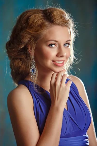 Portrait of charming girl with thick blond hair and blue eyes in a blue dress dress in the studio, close-up — Stock Photo, Image