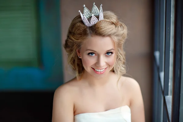 Close-up retrato de uma jovem mulher loira sorridente com lábios cheios, vestindo um vestido branco e uma coroa na cabeça como uma princesa — Fotografia de Stock