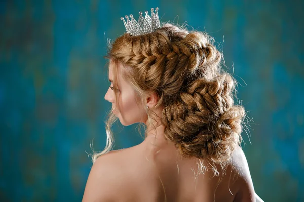 Retrato de uma jovem loira com cabelo grosso de luxo, trançada em uma trança, vestindo um vestido branco e uma coroa na cabeça, como uma princesa, vista da parte de trás — Fotografia de Stock