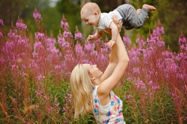 Yaz aylarında çim fireweed arka plan üzerinde erkek sevimli gülümseyen bebek kadar güzel ince sarışın anne atar