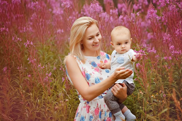 Bonito slim loira mãe abraços adorável sorrindo menino no fundo de grama fireweed no verão — Fotografia de Stock