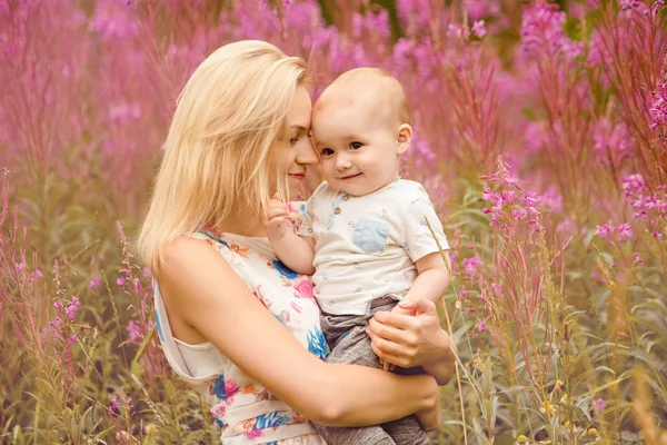Красивая стройная блондинка мама обнимает очаровательного маленького мальчика, на фоне травяного фейерверка летом — стоковое фото