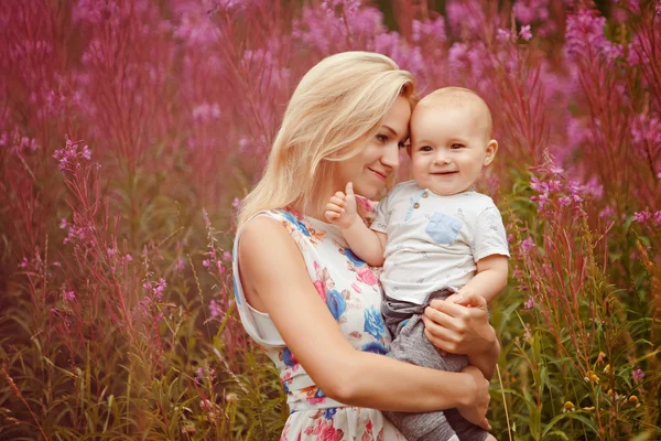 Bella magra mamma bionda abbraccia adorabile bambino, sullo sfondo di erba fireweed in estate — Foto Stock