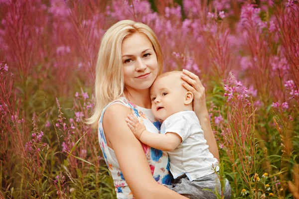 Bonito slim loira mãe abraços adorável menino, no fundo de grama fireweed no verão — Fotografia de Stock