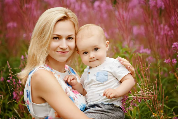 Retrato de uma bela mãe loira e adorável sorrindo menino no fundo da erva daninha no verão, close-up — Fotografia de Stock