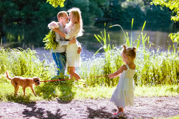 Muy linda niña rubia tira del perro por la correa en el fondo abrazando a los padres —  Fotos de Stock