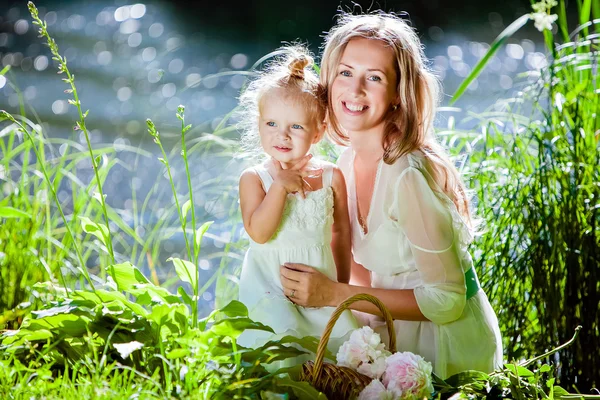 Máma a dcera šťastný úsměv na pozadí lesa a vody v podsvícení — Stock fotografie