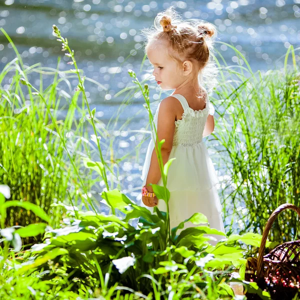 Schattig klein blonde meisje is backlit tegen de achtergrond van het water en gras — Stockfoto