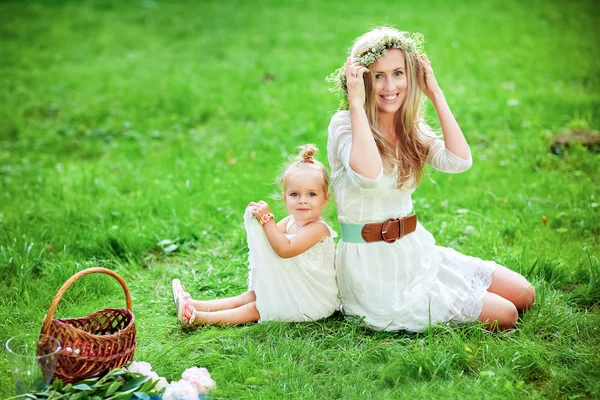 Mamá con una corona en la cabeza y su hija están sentadas en la hierba en el campo — Foto de Stock