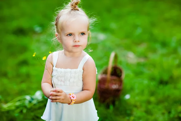 Χαριτωμένο μικρό ξανθό κορίτσι σε ένα λευκό φόρεμα που κατέχουν ένα λουλούδι στα χέρια του — Φωτογραφία Αρχείου