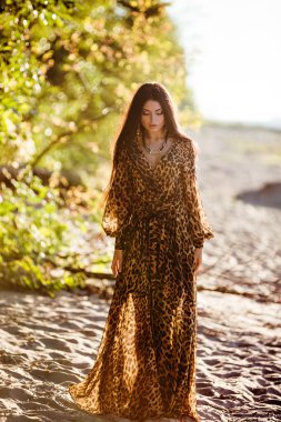 Sexy sensual beautiful brunette girl with long hair in leopard print dress, dancing on the sand