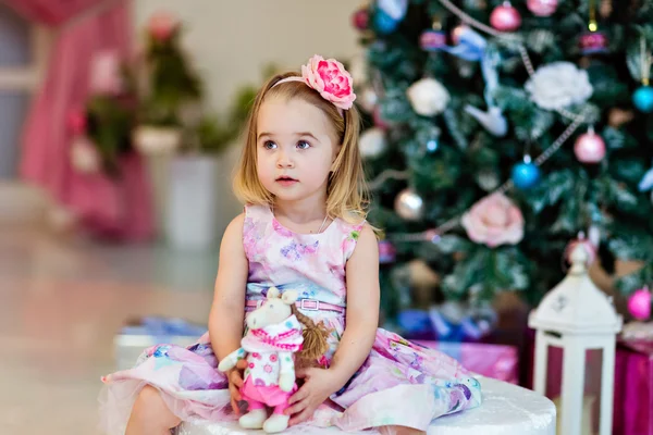 Uma criança pequena em um vestido de lavanda contra o fundo da árvore de Natal — Fotografia de Stock