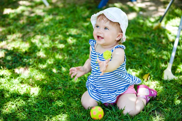 A little kid in the striped shirt is sitting on the grass — Φωτογραφία Αρχείου