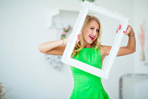 Beautiful blonde girl in a green dress holding frame and winks — ストック写真