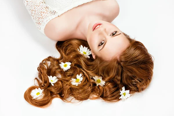 Retrato de una chica guapa y tierna pelirroja con margaritas en el pelo tumbadas en el suelo con los ojos cerrados, sobre un fondo blanco en Studio —  Fotos de Stock