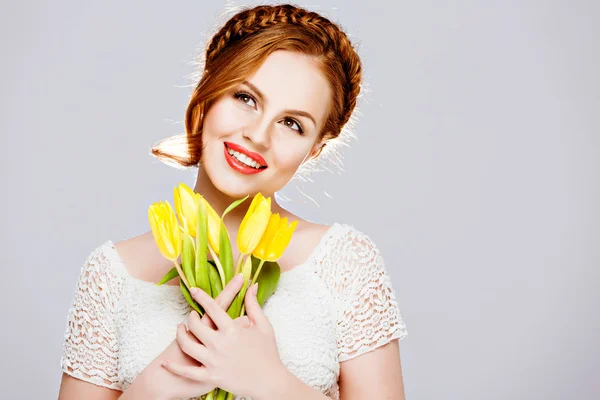 Menina bonita com cabelo vermelho em uma trança, mantém tulipas amarelas com olhos fechados no fundo branco no Studio — Fotografia de Stock