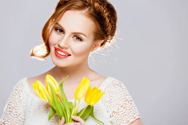 Menina bonita com cabelo vermelho em uma trança, mantém tulipas amarelas com olhos fechados no fundo branco no Studio — Fotografia de Stock