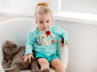Very cute little girl in the blue jacket sits on the chair with 