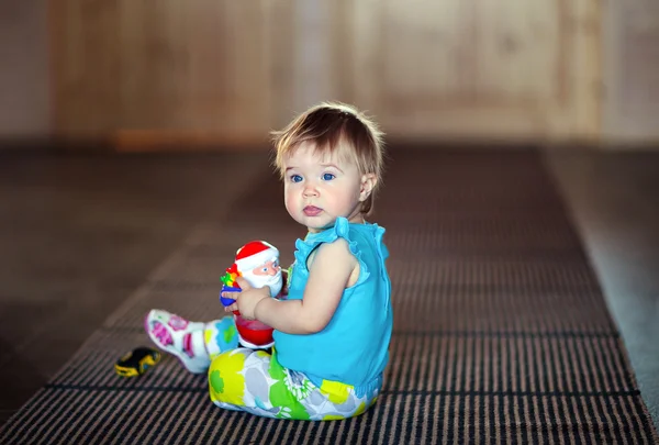 Cute little girl sitting on the floor and holding a toy Santa Cl — 스톡 사진