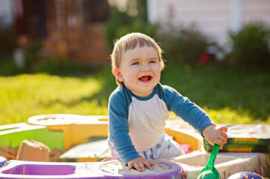 Küçük tombul bebek çocuk gülüyor, yaz aylarında güneşli hava kum havuzunda oturuyor