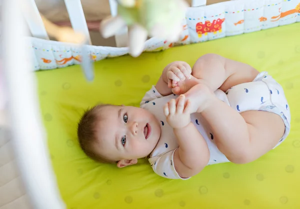 A charming little boy lying in bed and holding hands over his le — Stock Photo, Image