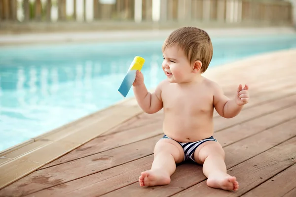 Pequeño niño sentado cerca de la piscina y está sosteniendo el sol — Foto de Stock