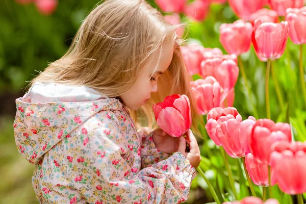 Heel schattig mooi meisje blonde in roze jas kosten rond bloem — Stockfoto