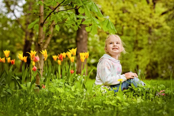 Menina loira bonita muito doce senta-se perto do canteiro de flores de vermelho — Fotografia de Stock